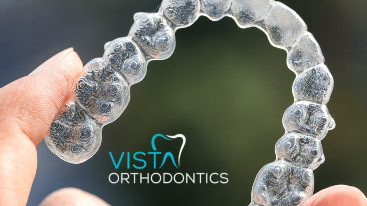 A clear aligner held up in front of the Vista Orthodontics logo