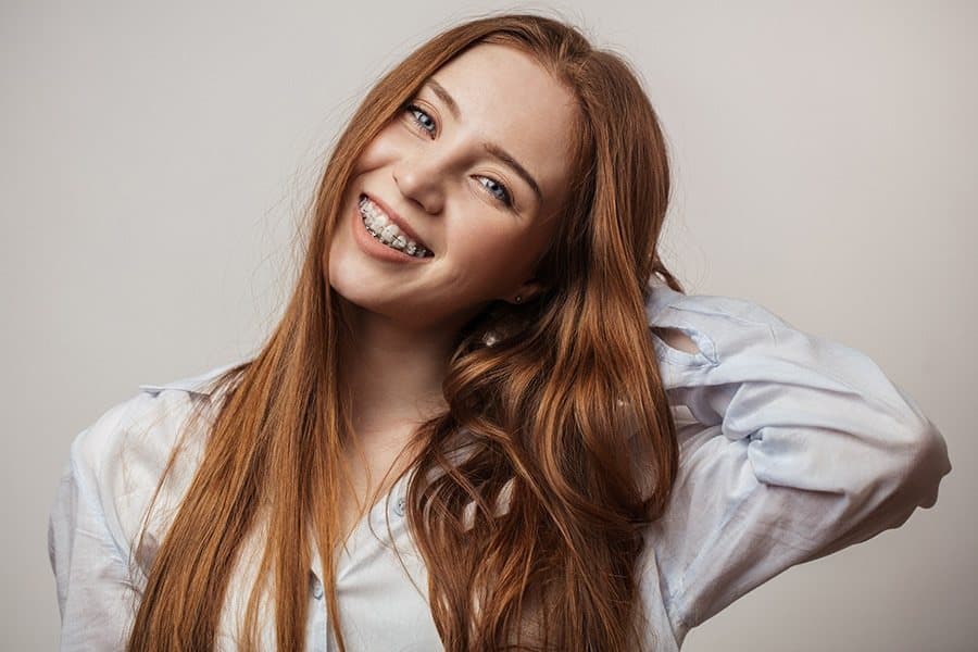 A smiling person wearing clear ceramic braces