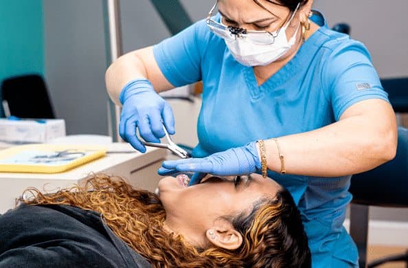 A Vista Orthodontics clinician in blue scrubs using orthodontic pliers to adjust braces for a patient reclined in the treatment chair