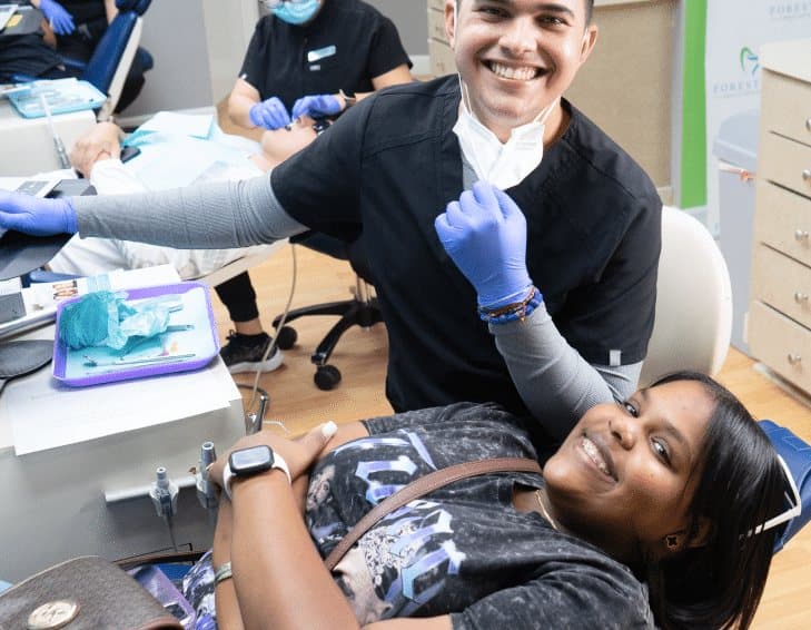 A smiling Vista Orthodontics clinician in gloves beside a smiling patient with braces reclined in the treatment chair